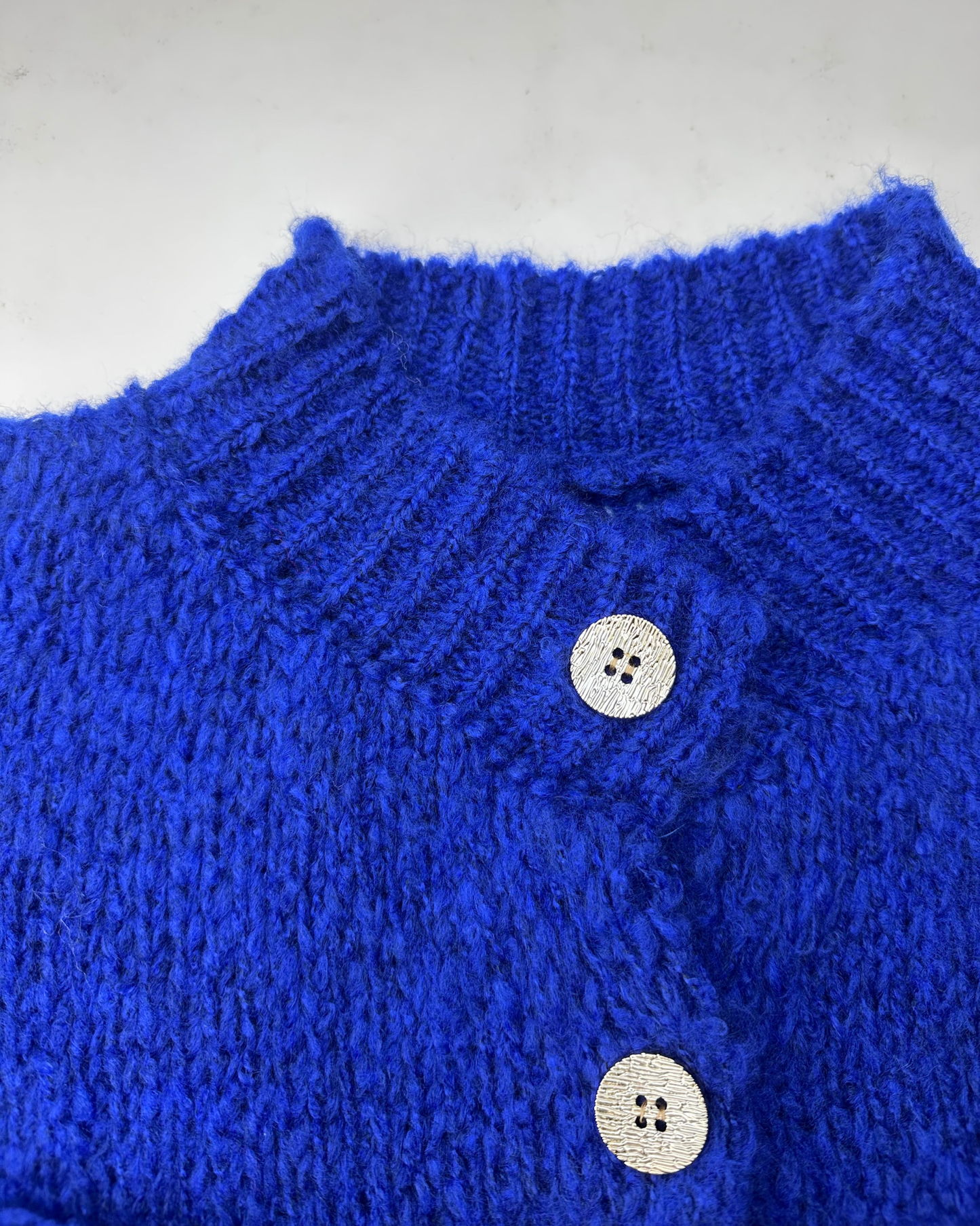 Nahaufnahme des königsblauen, gerippten Kragens und der glänzenden Knöpfe des Cardigans.