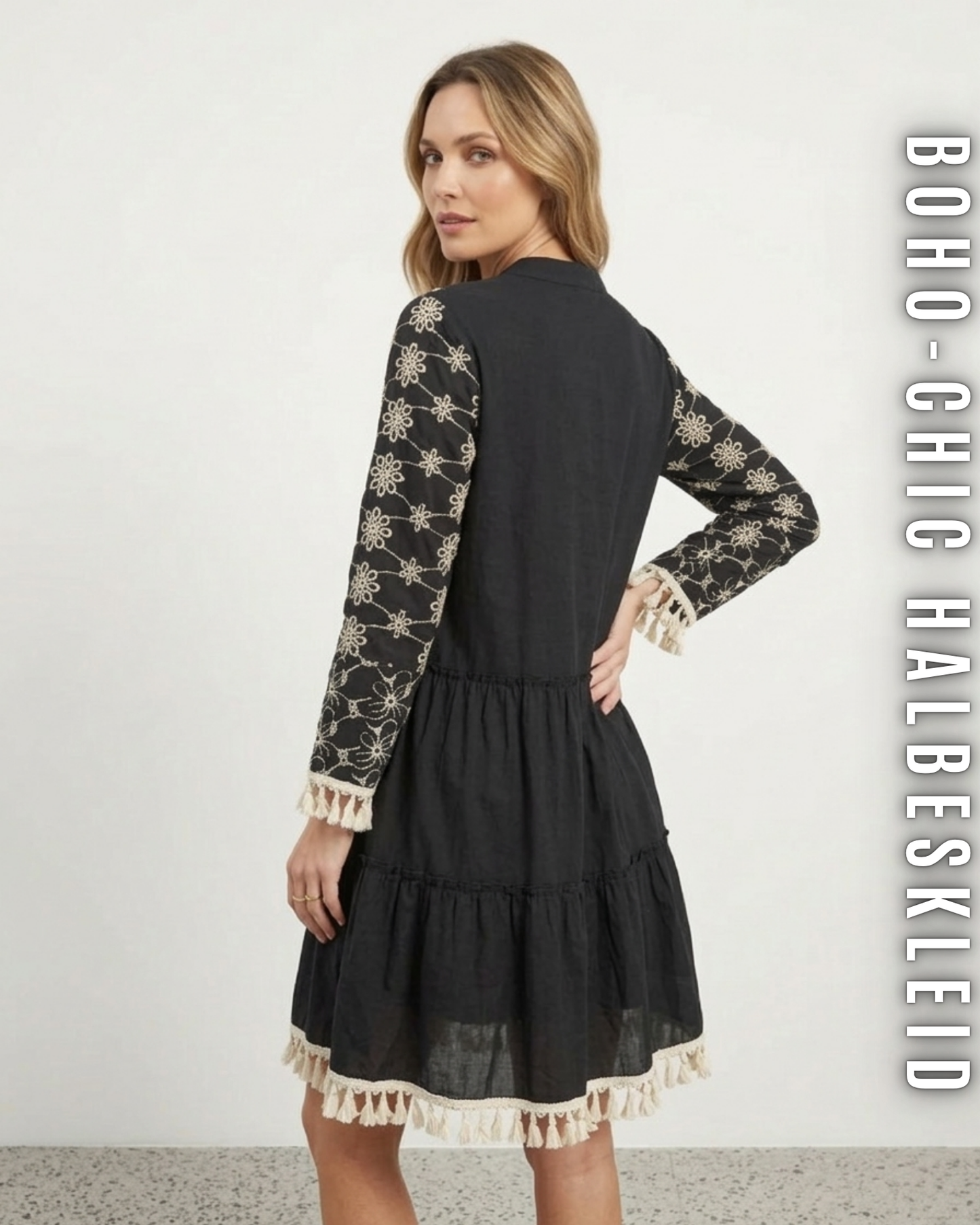 Nahaufnahme Rückseite schwarzes Stufenkleid vor weißem Hintergrund, Details der cremefarbenen Quasten-Fransen an Ärmeln und Saum.