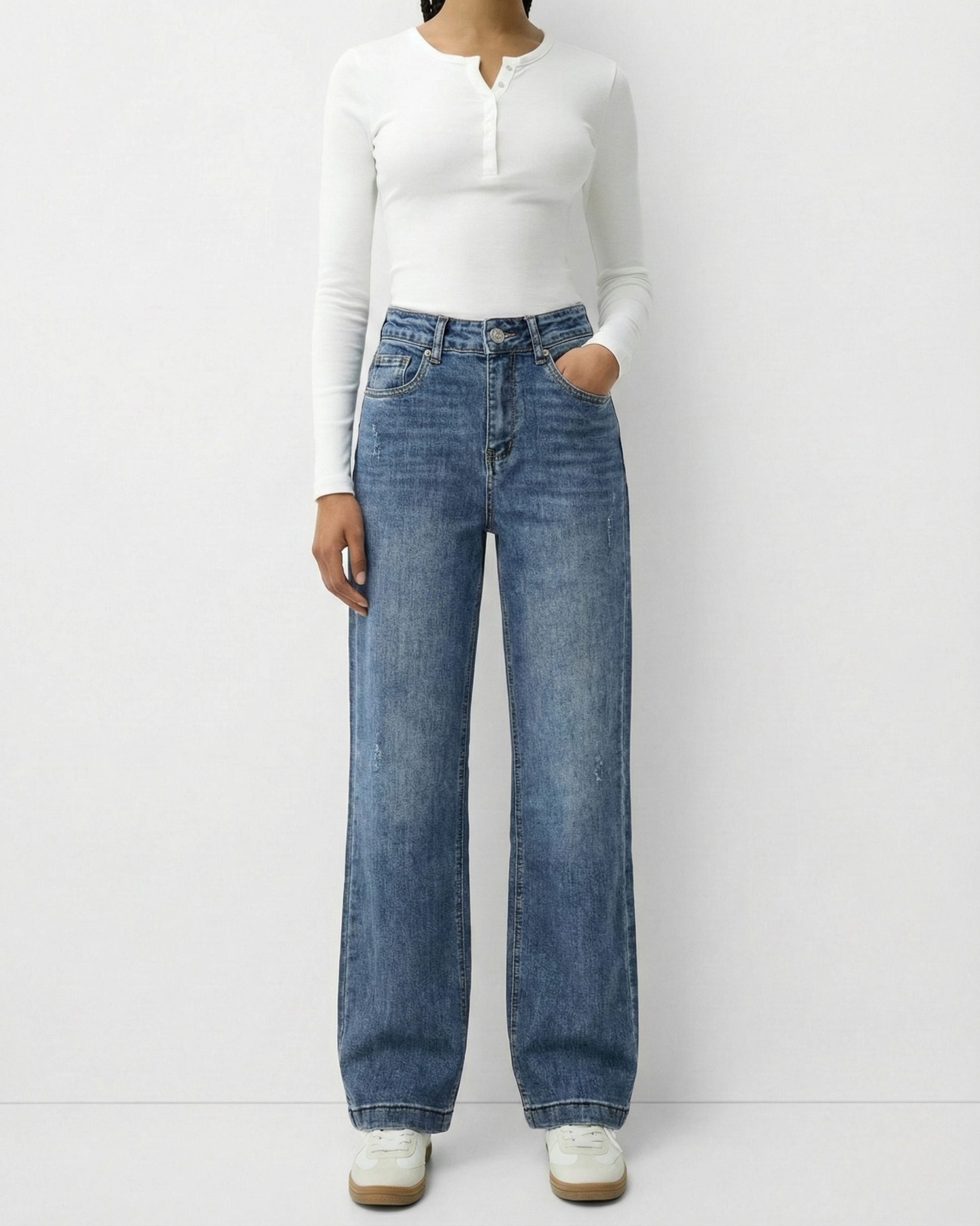 Frau trägt eine mittelblaue High-Waist Straight Leg Jeans kombiniert mit einem weißen Langarmshirt.