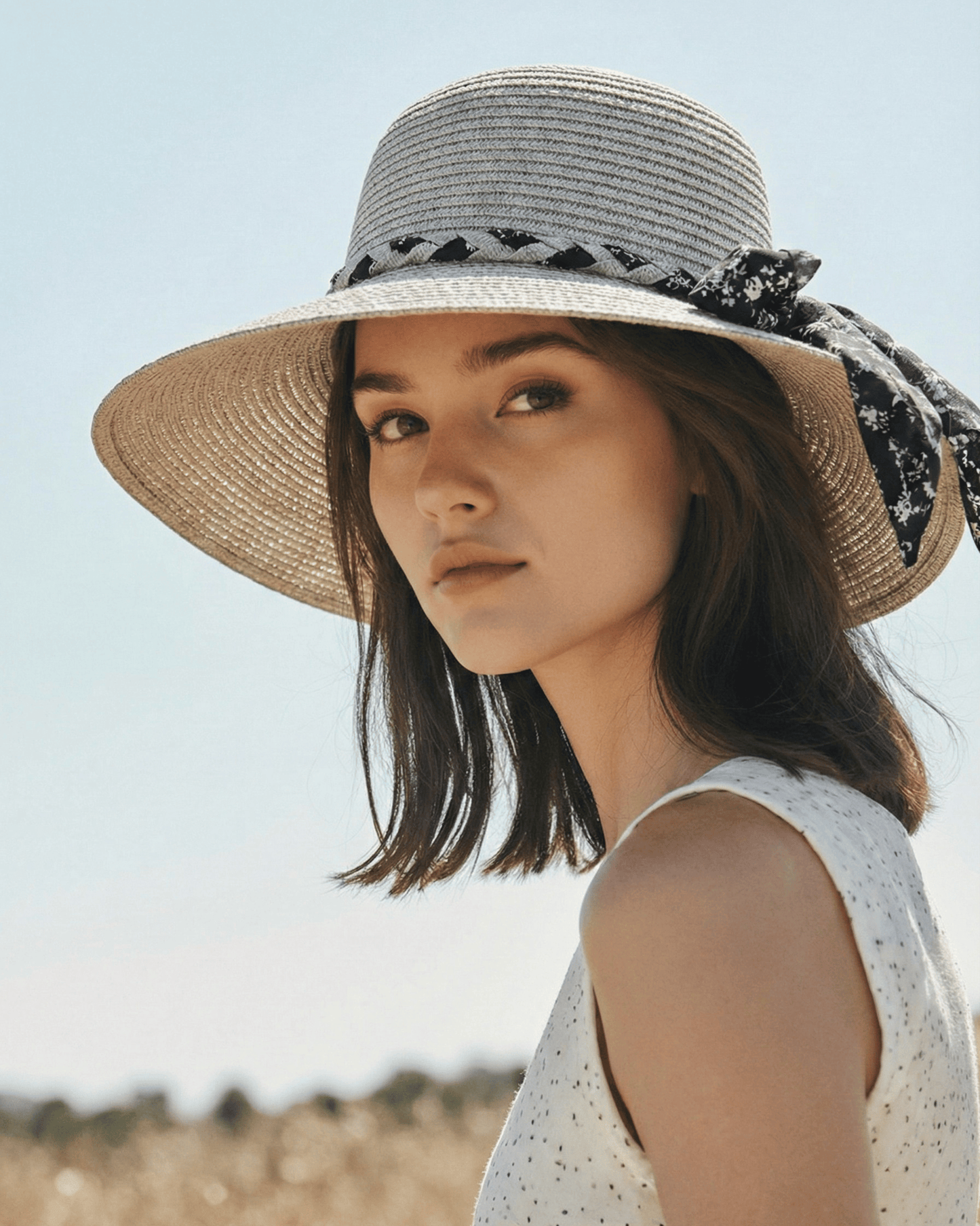 Ein Model trägt den hellen Strohhut als Sonnenschutz am Strand.