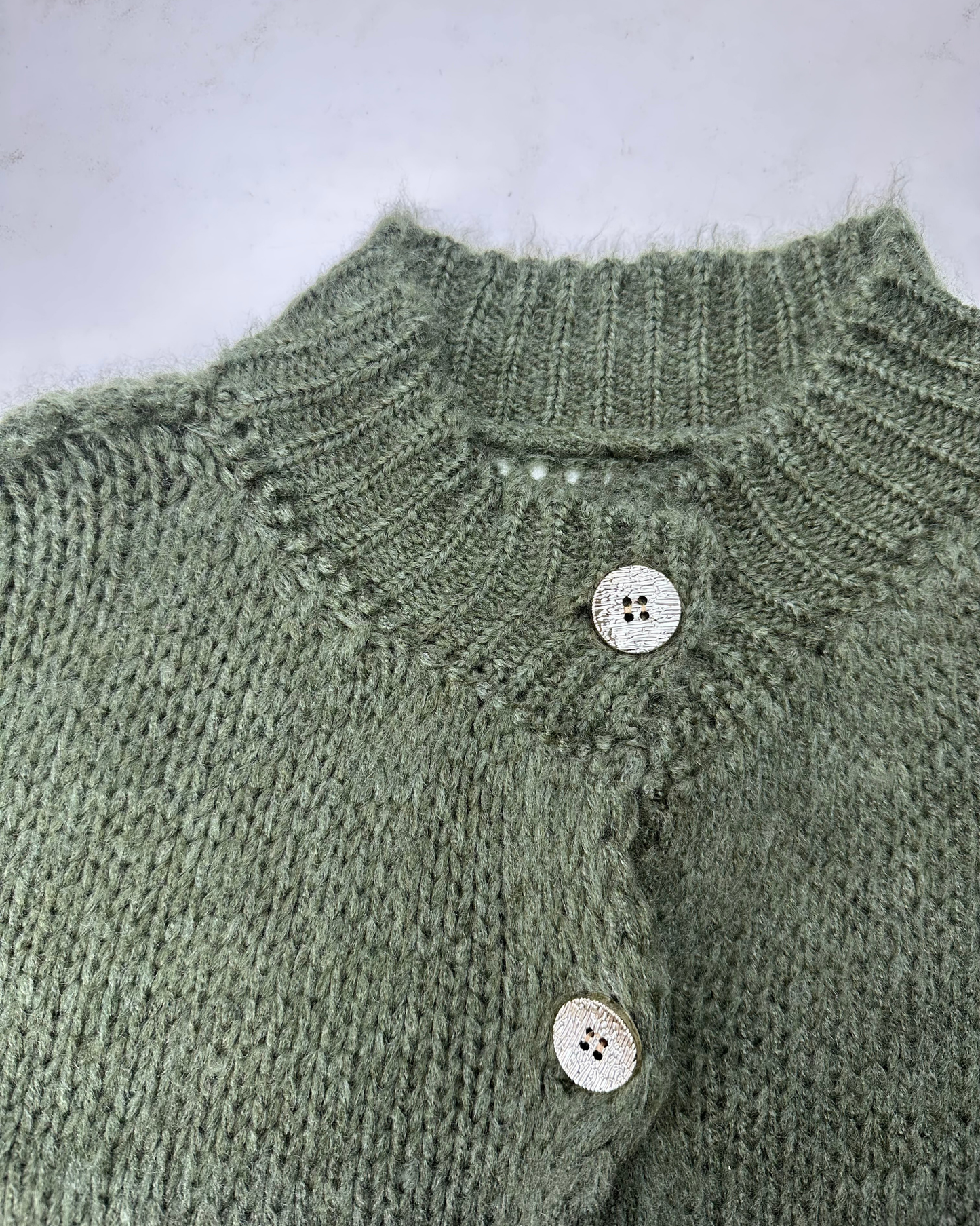 Nahaufnahme des oliven, gerippten Kragens und der glänzenden Knöpfe des Cardigans.