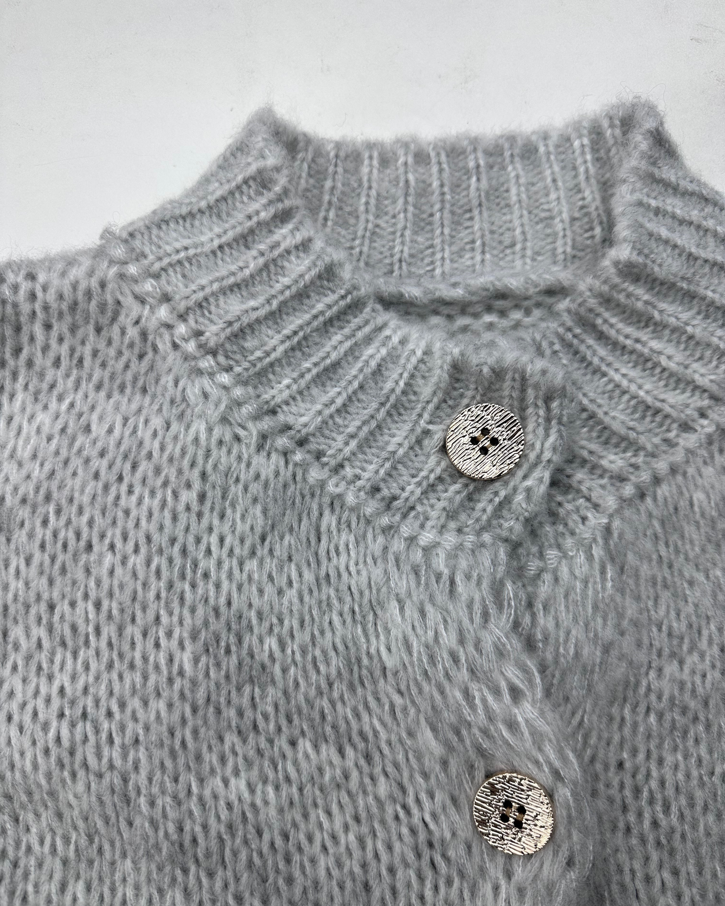 Nahaufnahme des hellgrauen, gerippten Kragens und der glänzenden Knöpfe des Cardigans.