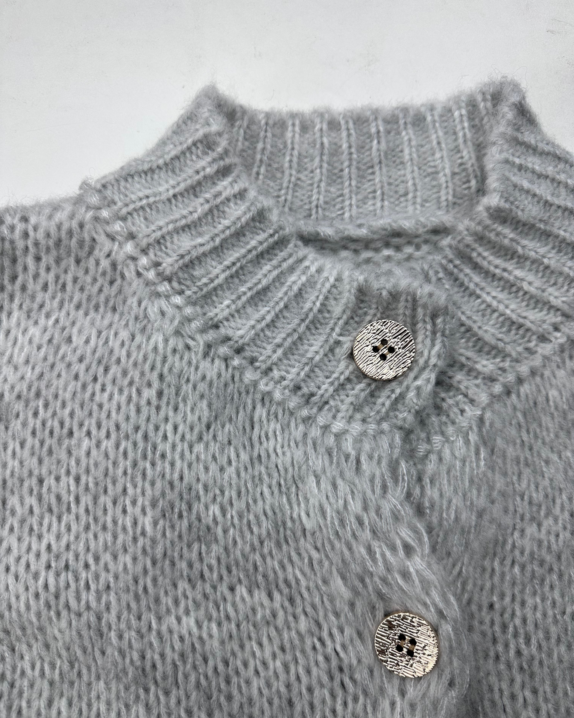 Nahaufnahme des hellgrauen, gerippten Kragens und der glänzenden Knöpfe des Cardigans.