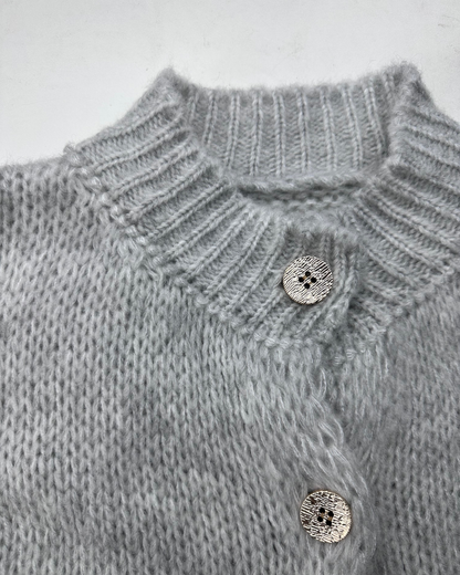 Nahaufnahme des hellgrauen, gerippten Kragens und der glänzenden Knöpfe des Cardigans.