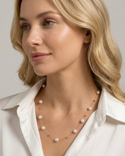 Nahaufnahme einer blonden Frau im weißen Hemd, die die elegante, goldene Halskette mit den schimmernden Perlen trägt.