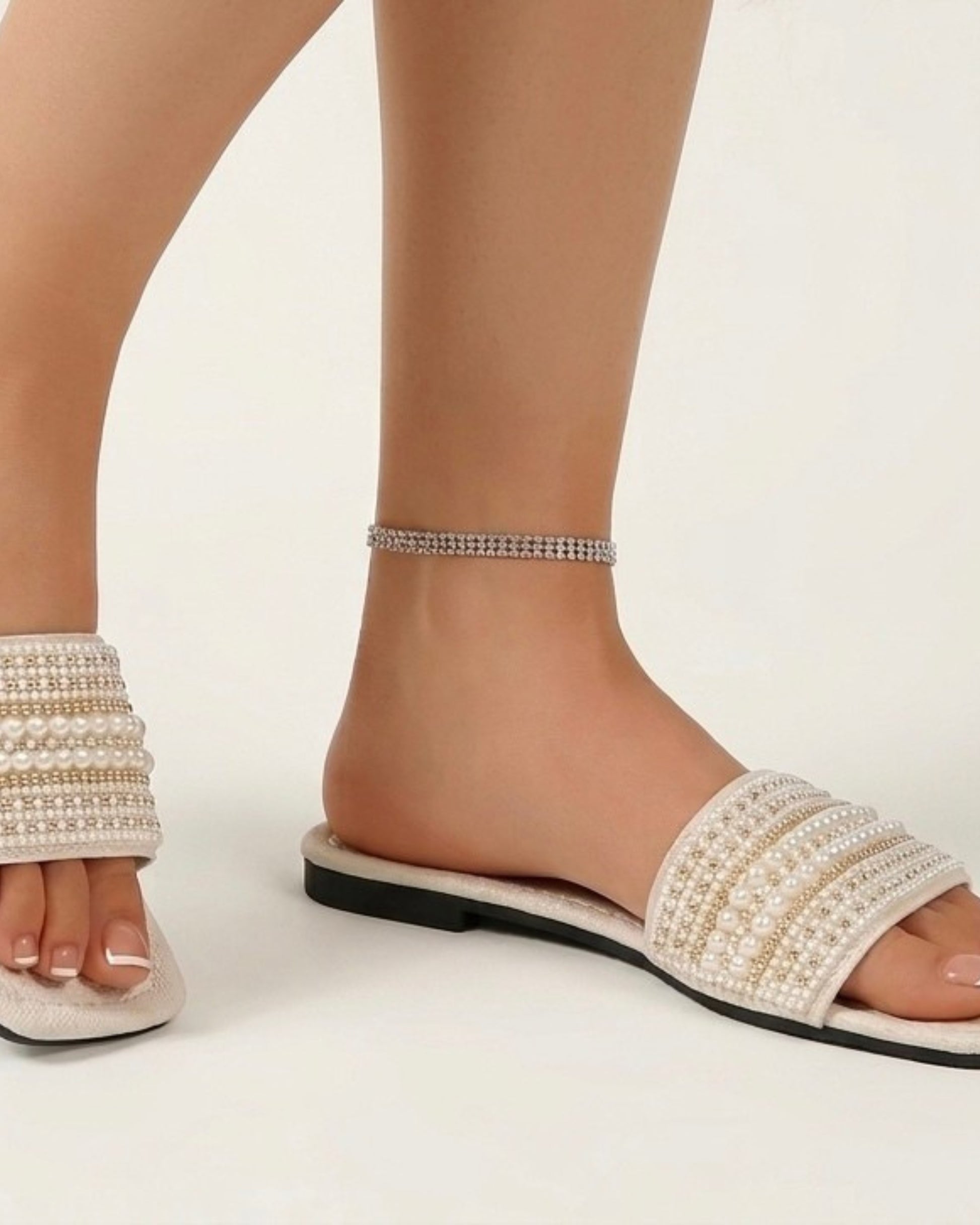 Nahaufnahme der Strass- und Perlenreihen auf dem breiten Riemen der flachen Sommer-Mules beim Tragen.
