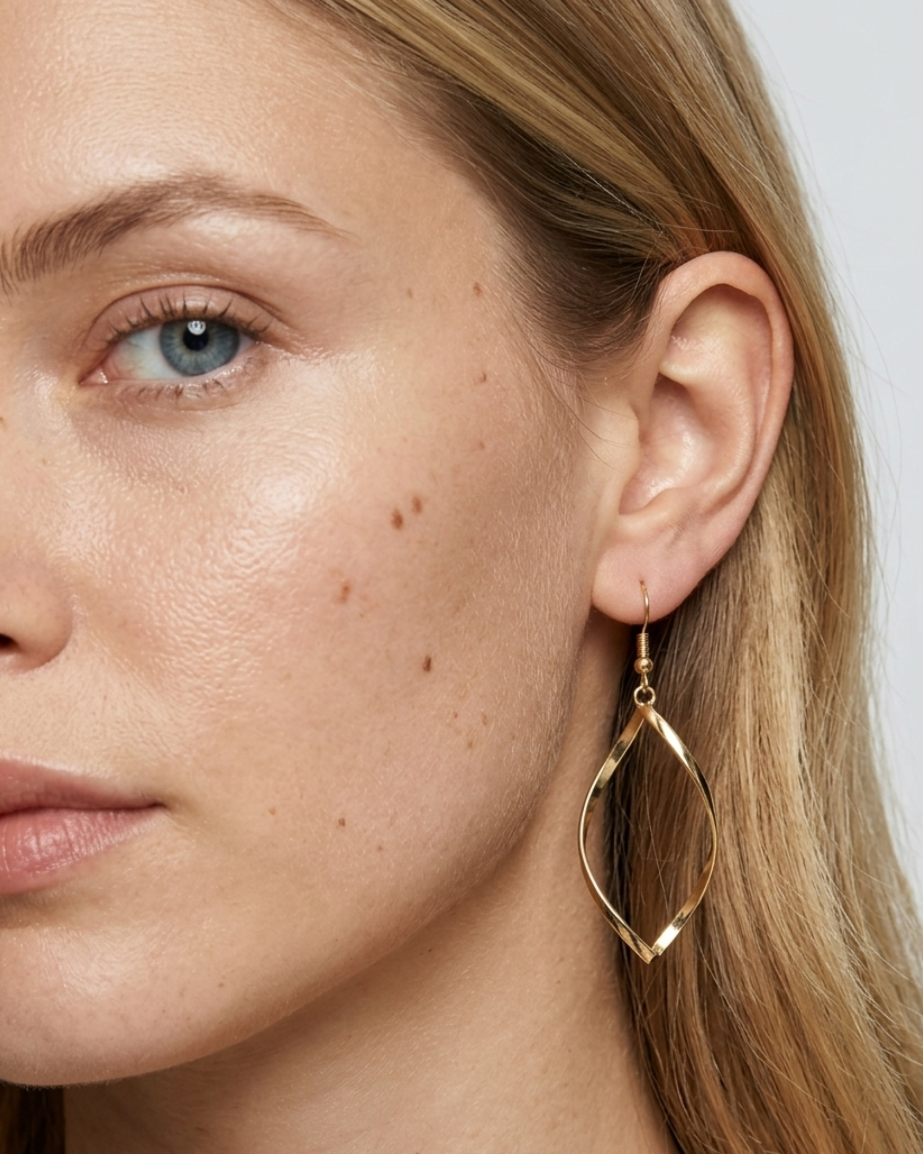Nahaufnahme eines ELEXUA TWIST Twisted-Hängeohrrings in Gold am Ohr eines Models.