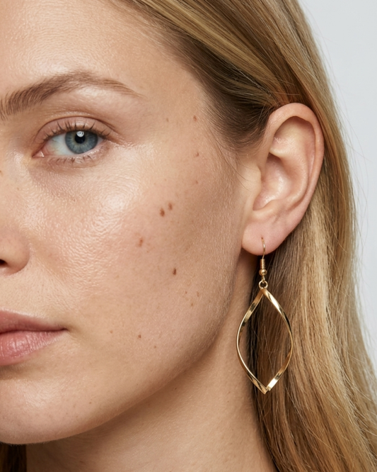 Nahaufnahme eines ELEXUA TWIST Twisted-Hängeohrrings in Gold am Ohr eines Models.