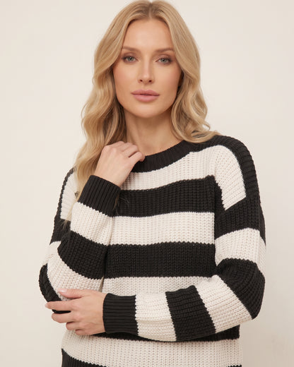 Nahaufnahme eines schwarz-weiß gestreiften Damenpullovers aus grobem Strick. Das blonde Model verschränkt leicht die Arme, wodurch die weiche Struktur des Strickmusters und die Rippbündchen an den Handgelenken sowie der klassische Rundhalsausschnitt im Detail sichtbar werden.