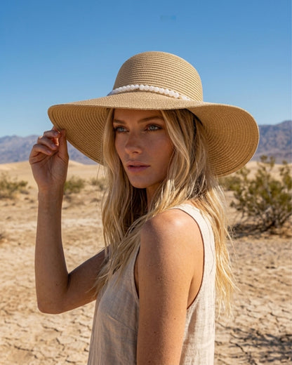 Seitenprofil einer blonden Frau in einer sonnigen Wüstenlandschaft, die den eleganten beigen Strohhut mit dem weißen Perlenband präsentiert.