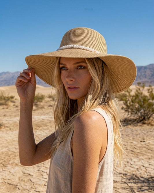 Seitenprofil einer blonden Frau in einer sonnigen Wüstenlandschaft, die den eleganten beigen Strohhut mit dem weißen Perlenband präsentiert.