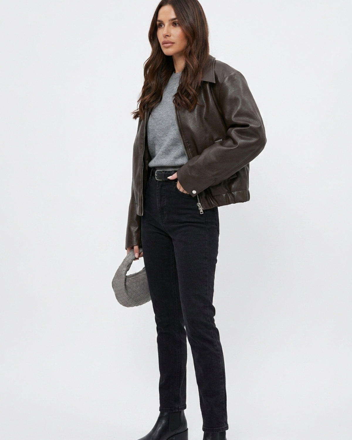 Lederjacke im Layering-Look über grauem Strickpullover und schwarzer High-Waist-Jeans