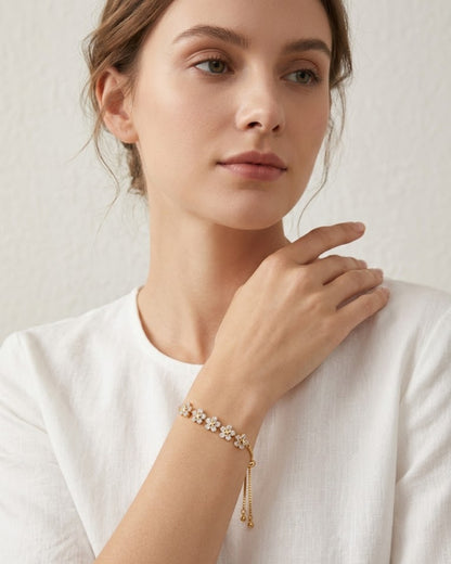 Nahaufnahme einer Frau in einem weißen Leinenoberteil, die das filigrane goldene Blüten-Armband mit funkelnden Zirkonia-Steinen am Handgelenk trägt.
