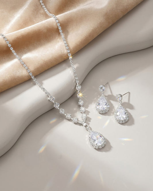 Detailaufnahme der versilberten Riviera-Kette und Ohrringe mit funkelndem Birnenschliff-Anhänger auf einer eleganten Marmorplatte.